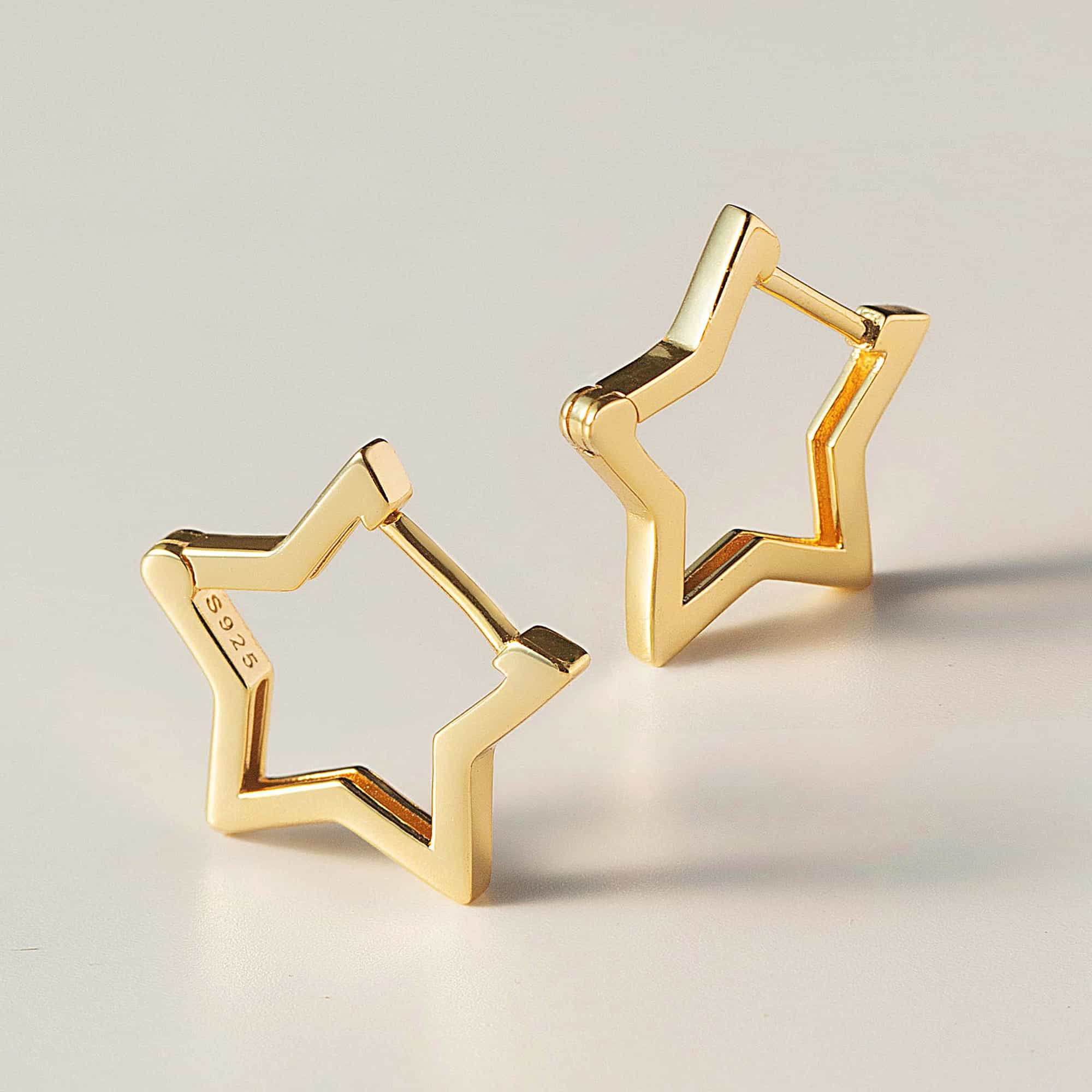 Gold vermeil open star-shaped small hoop earrings, shown at an angle on a cream surface