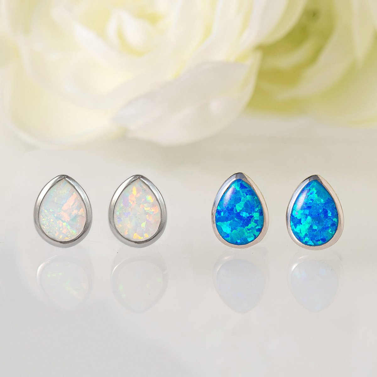 Pairs of sterling silver pear bezel studs with white and blue stones, on a pale surface