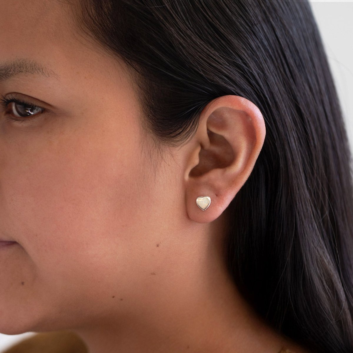 Sterling silver heart bezel stud with a white iridescent stone, shown on a model's lobe
