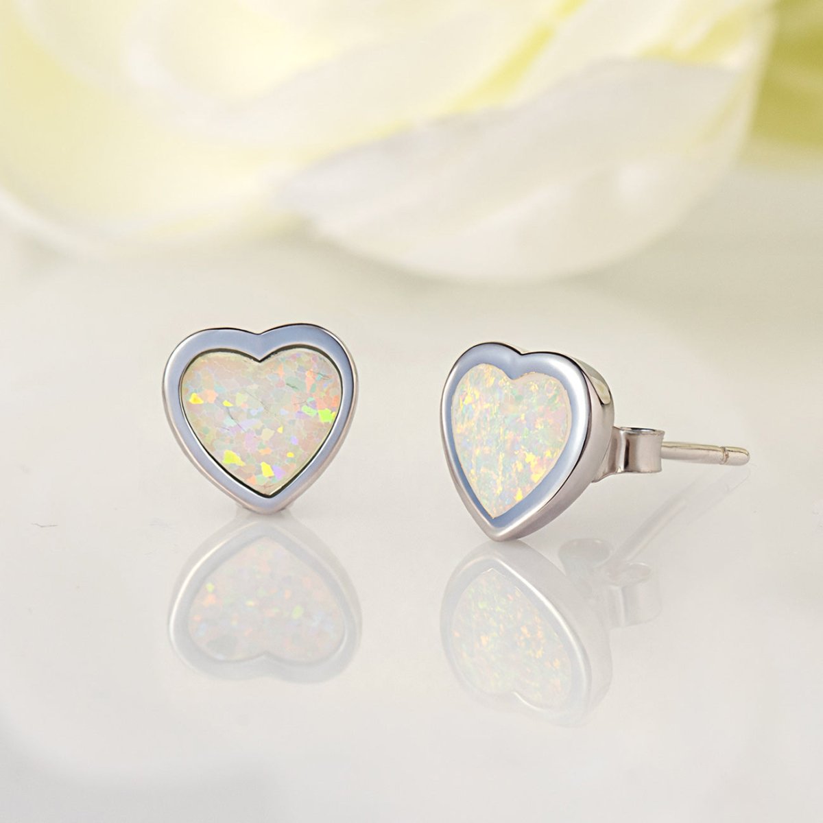 Sterling silver heart bezel studs with white iridescent stones, on a glossy surface
