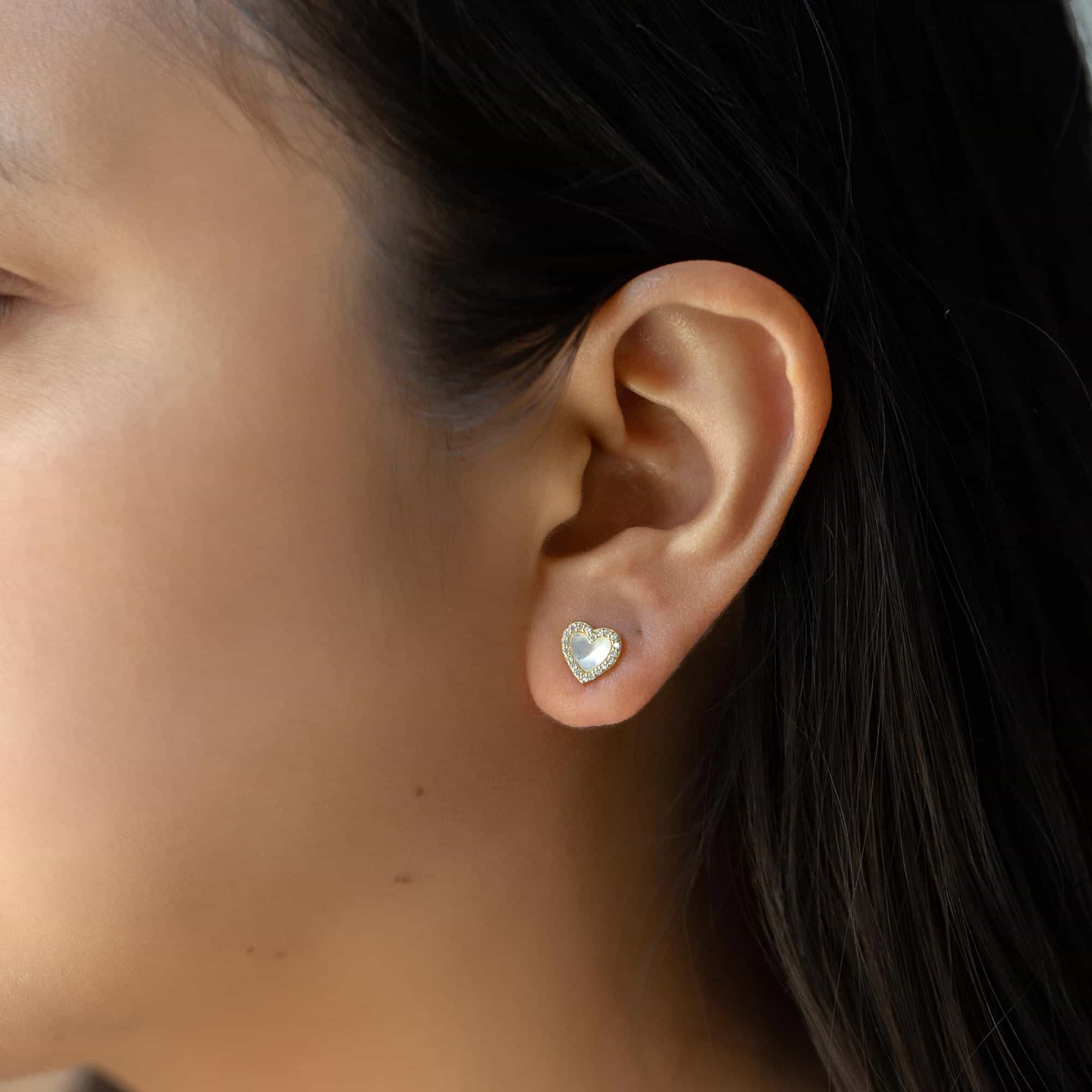 Gold vermeil mother of pearl halo heart stud with a pavé outline, shown on a model's ear