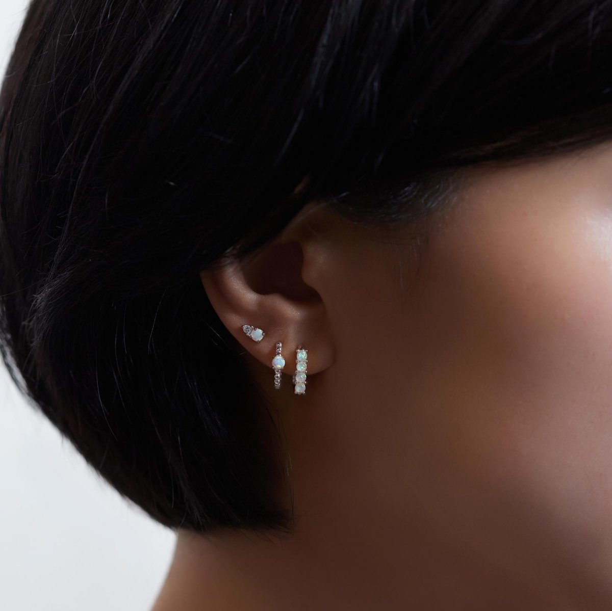 Sterling silver white opal huggie hoops and beaded huggie shown on a model's lobe