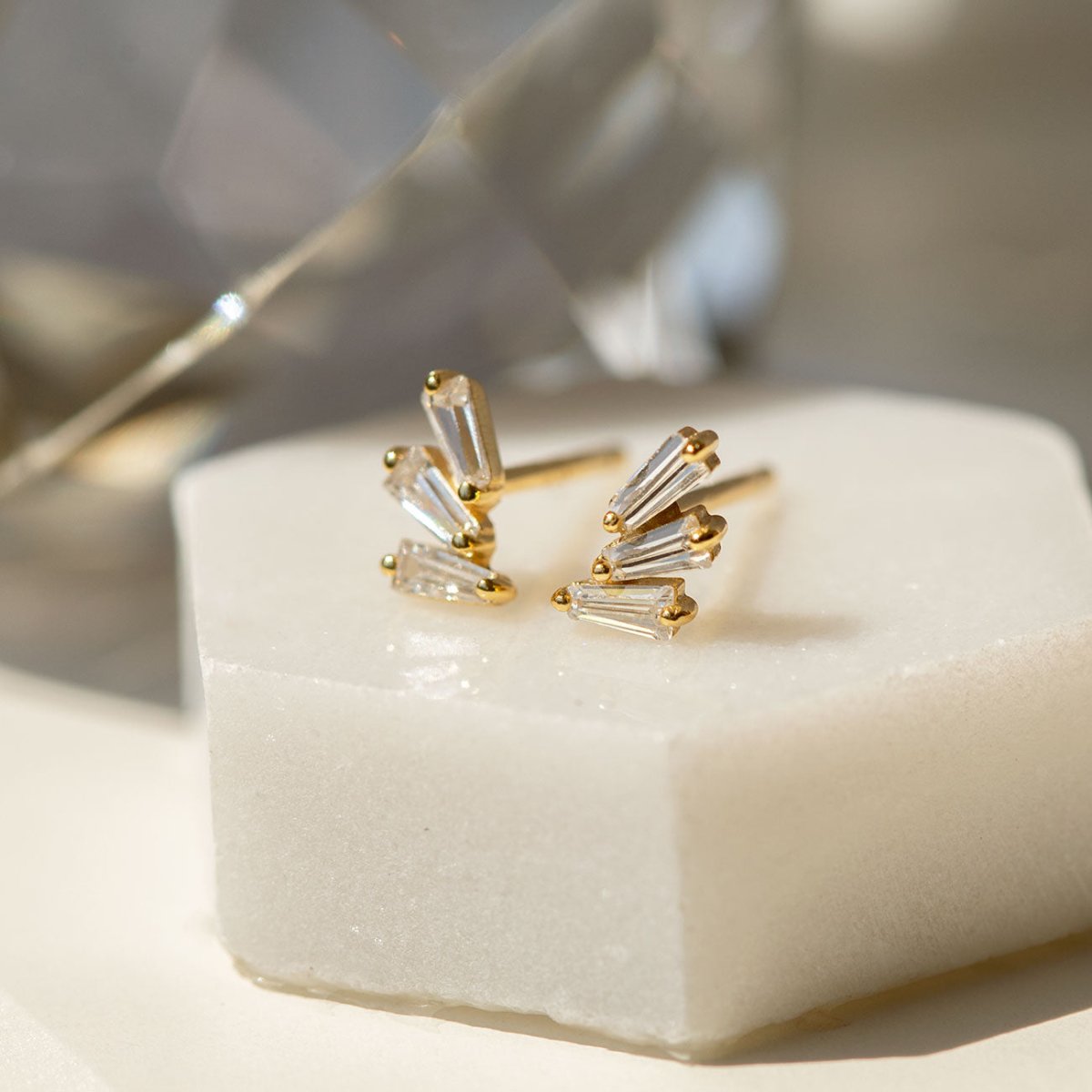 Gold vermeil fanned baguette stud earrings with clear stones, close-up detail on white marble