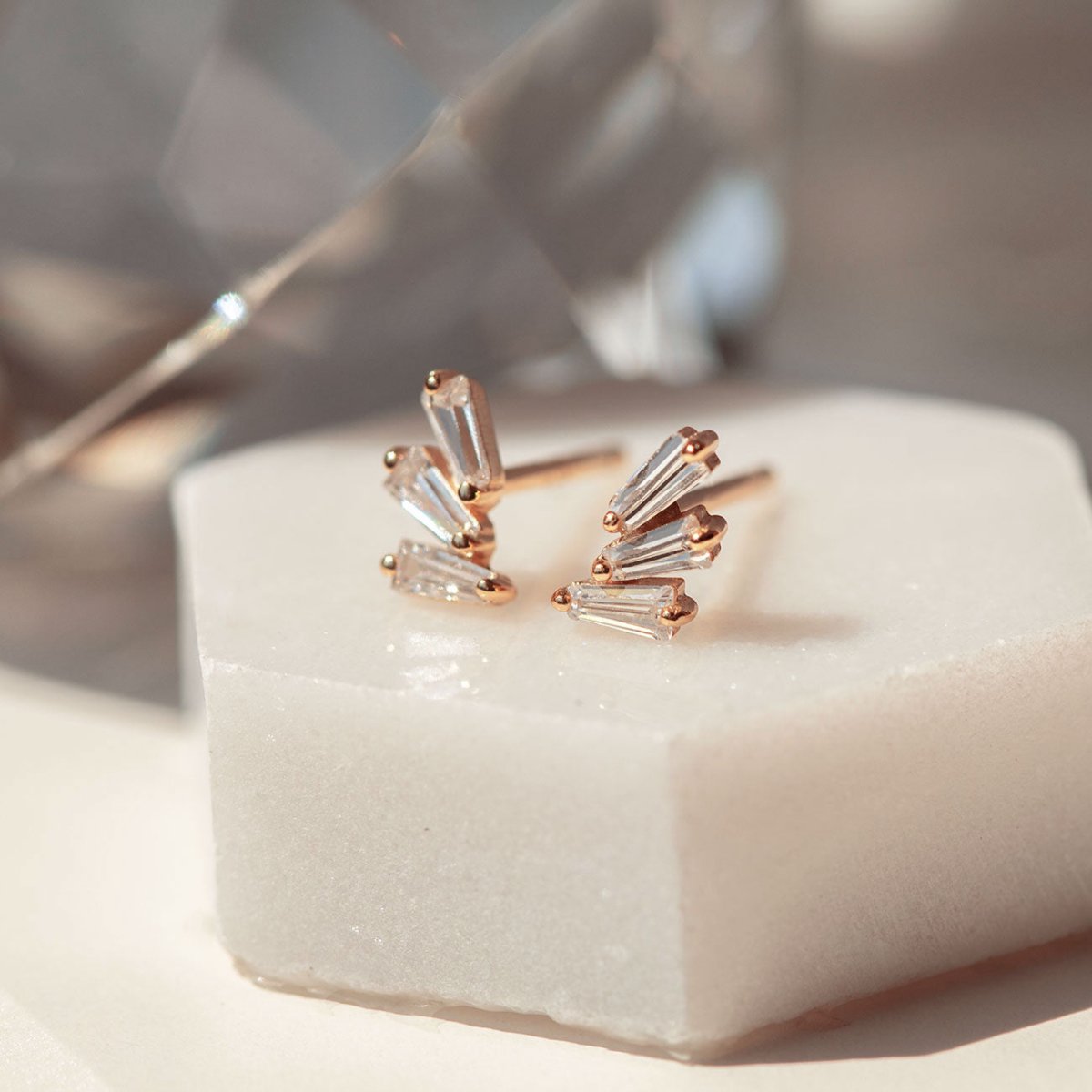 Rose gold vermeil fanned baguette stud earrings with clear stones, close-up on white marble