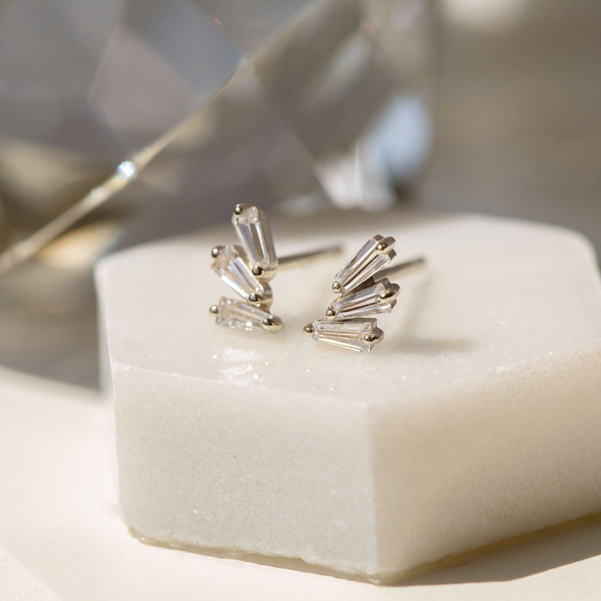 Sterling silver fanned baguette stud earrings with clear stones, close-up detail on white marble