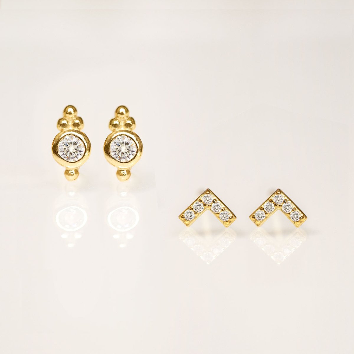 Gold vermeil pavé chevron studs styled beside bezel round clear-stone studs, on a cream background