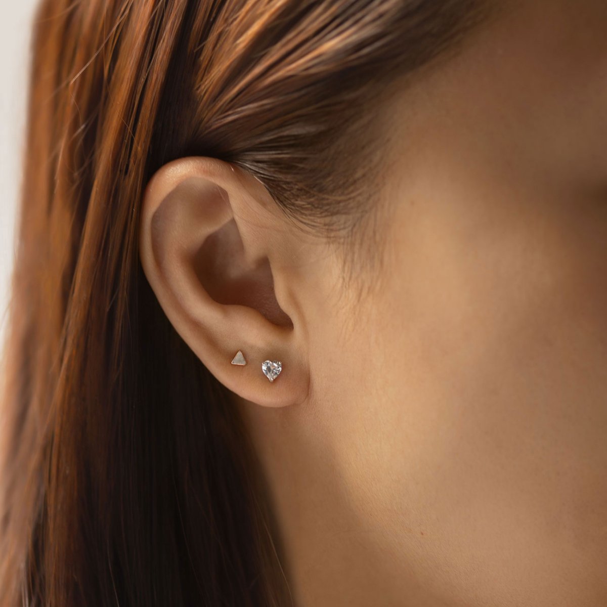 14K white gold heart-cut white zirconia stud shown on a model's earlobe beside a triangle stud