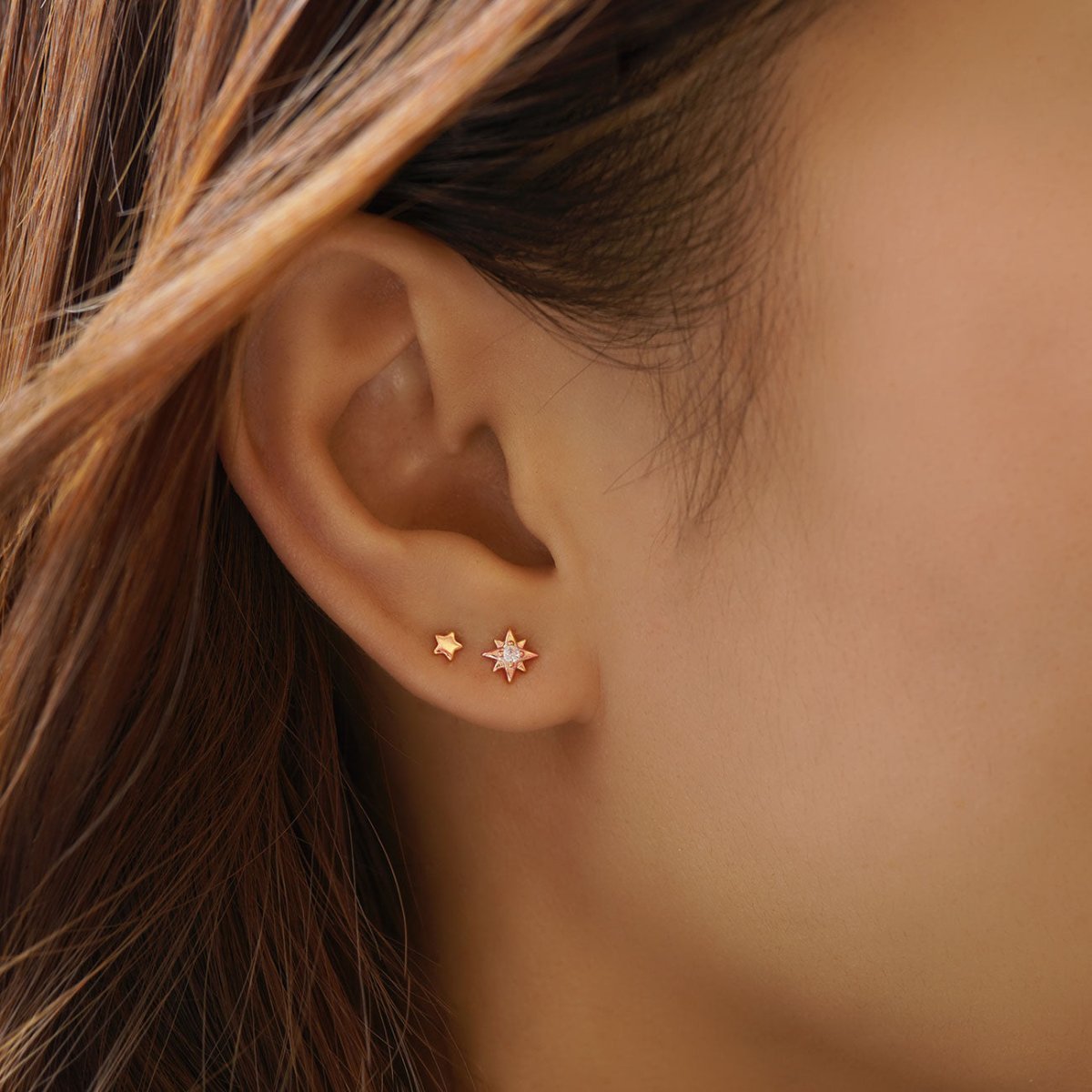 Rose gold vermeil starburst and plain star studs with a white zirconia center, shown on a model's lobe