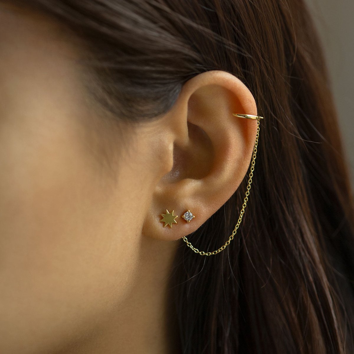 Gold vermeil sunburst star stud shown in a model's lobe with a clear stone stud and ear cuff