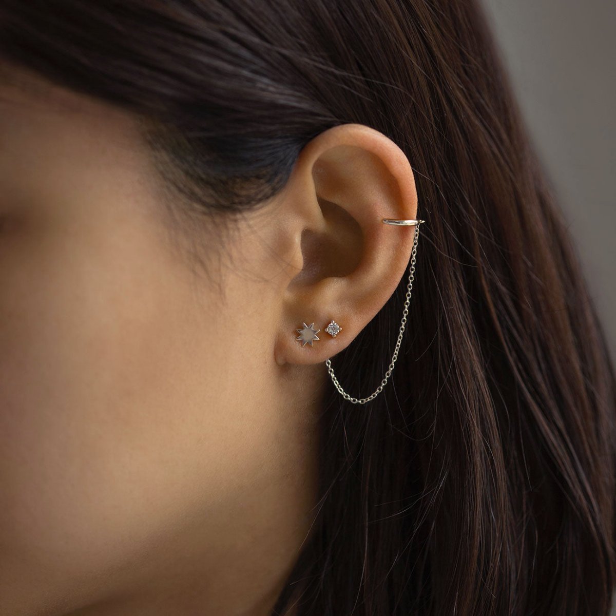 Sterling silver starburst stud with a small clear stone, shown on a model's lobe with an ear chain