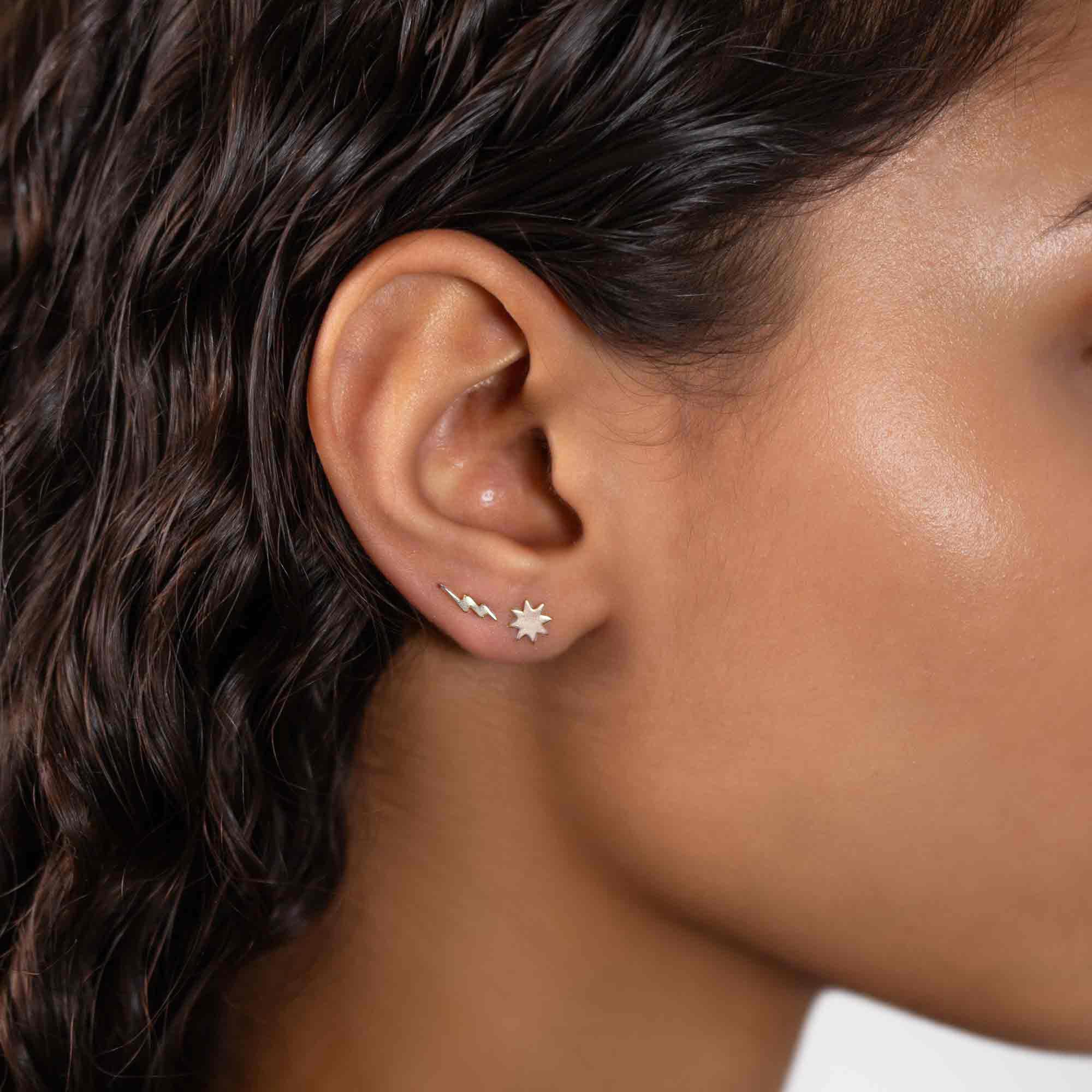 Sterling silver lightning bolt and starburst stud earrings shown on a model's lobe