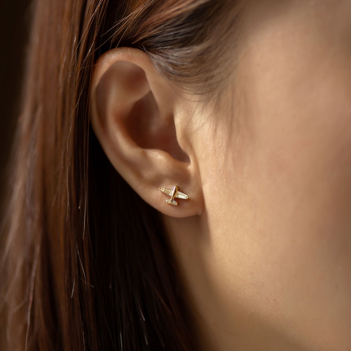 Gold vermeil airplane stud with a clear stone, shown in a lobe piercing on a model's ear