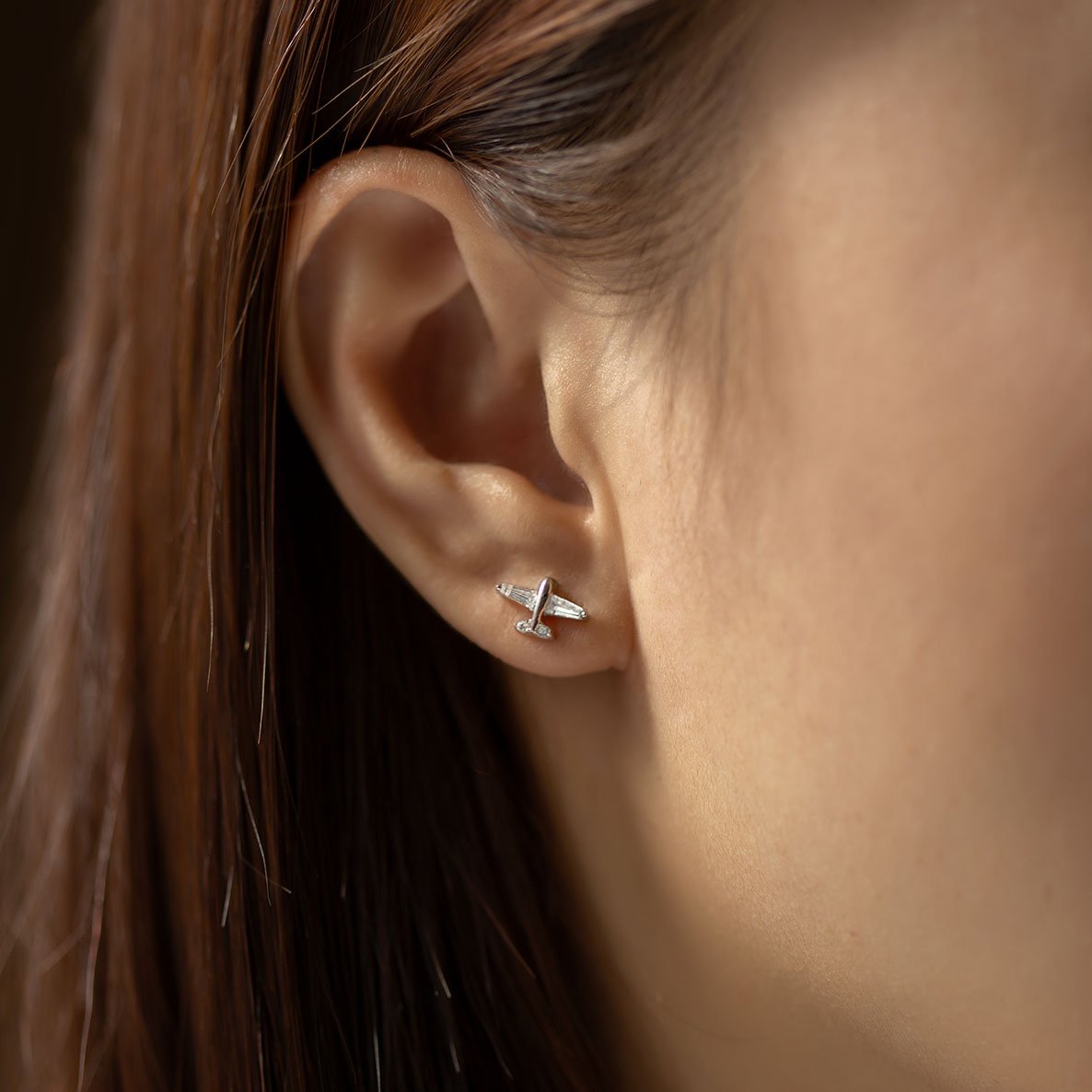 Sterling silver airplane stud with a clear stone, worn in a lobe piercing on a model's ear