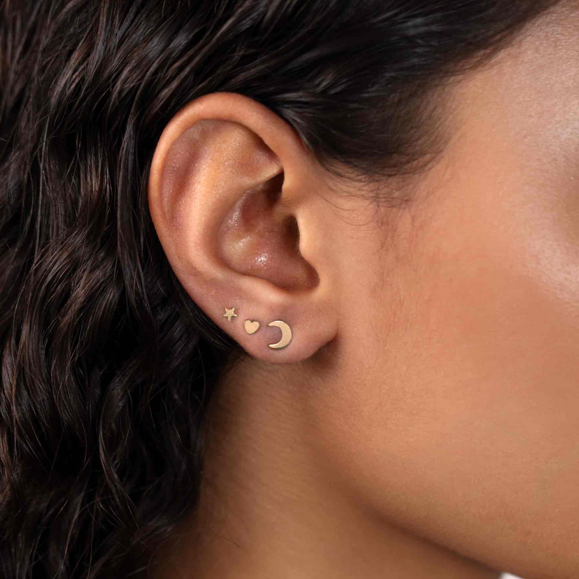 Gold vermeil tiny heart stud worn on a model's lobe with star and crescent moon studs
