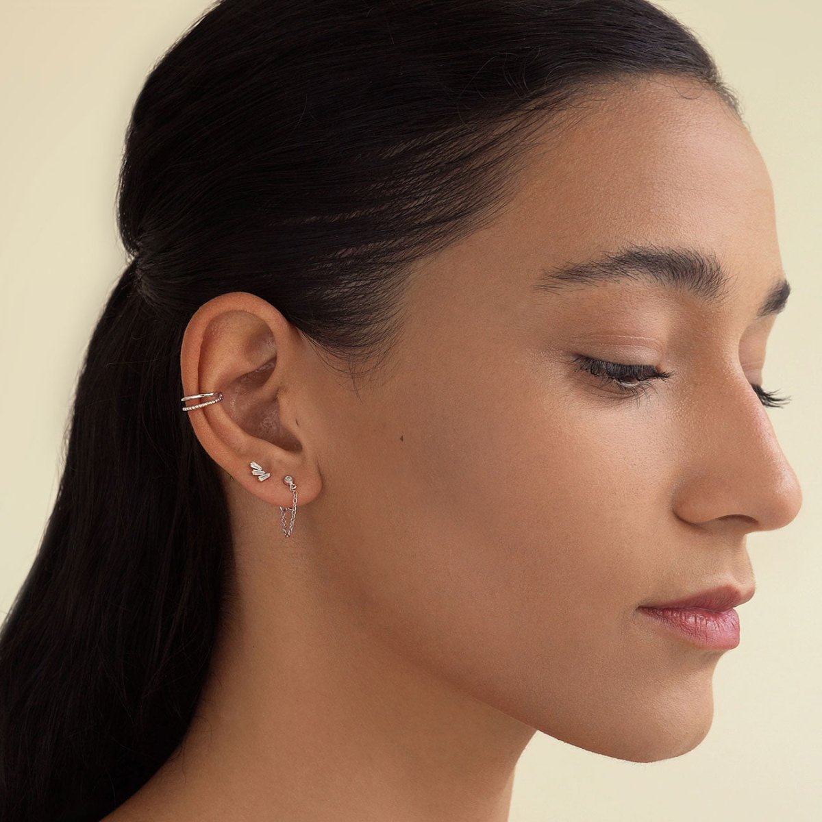 Sterling silver double ear cuff worn on the upper ear above stud and chain earrings, on a model's ear