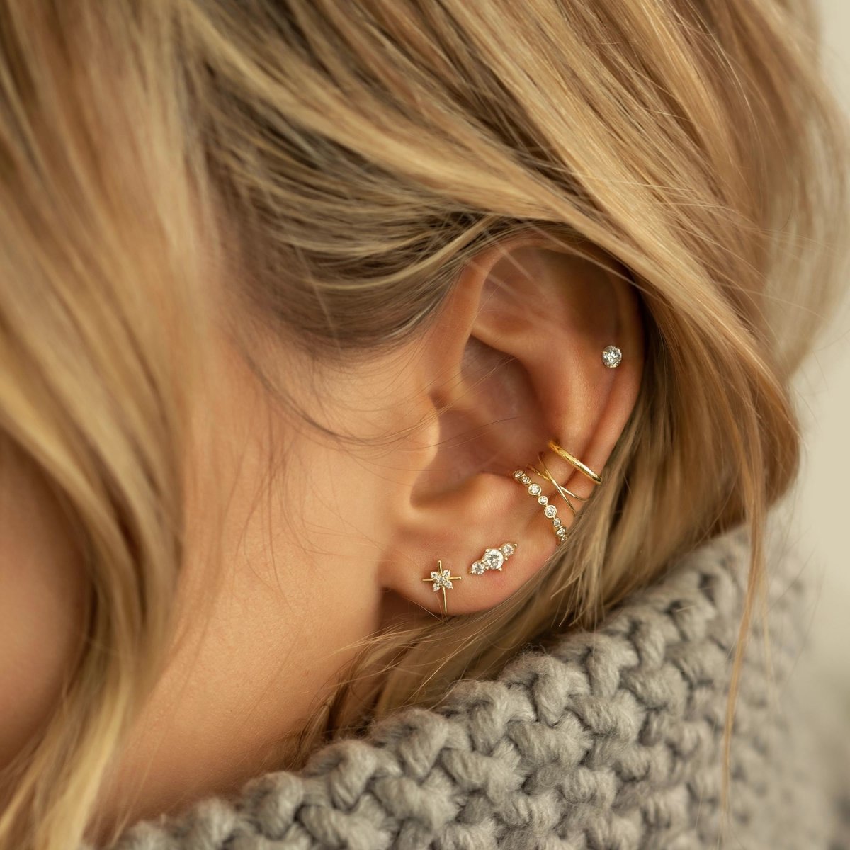 14K gold thin cross stud earring with clear zirconia stones, shown on a model's lobe