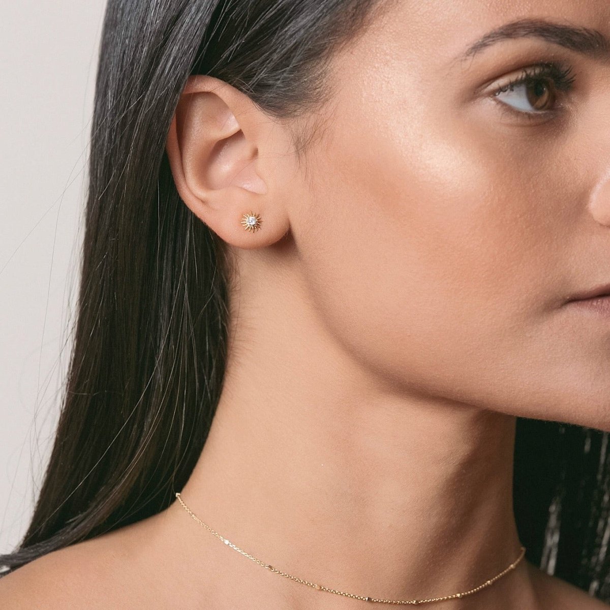 Gold vermeil sunburst stud with a clear stone shown on a model's lobe, with a fine gold chain necklace
