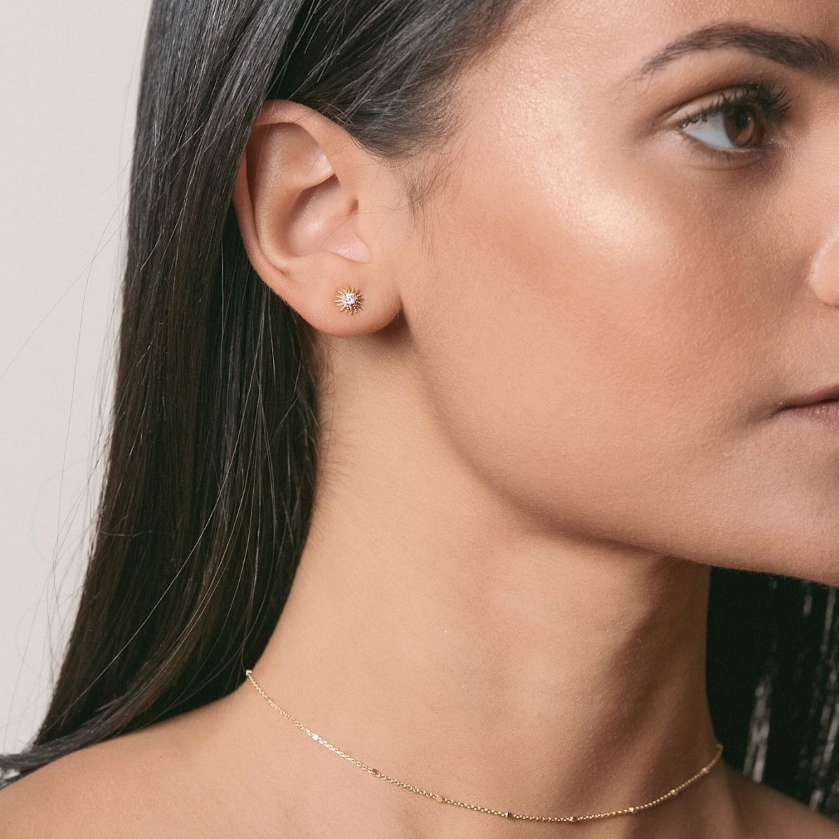 Sterling silver sunburst stud with a clear stone shown on a model's lobe, with a fine chain necklace