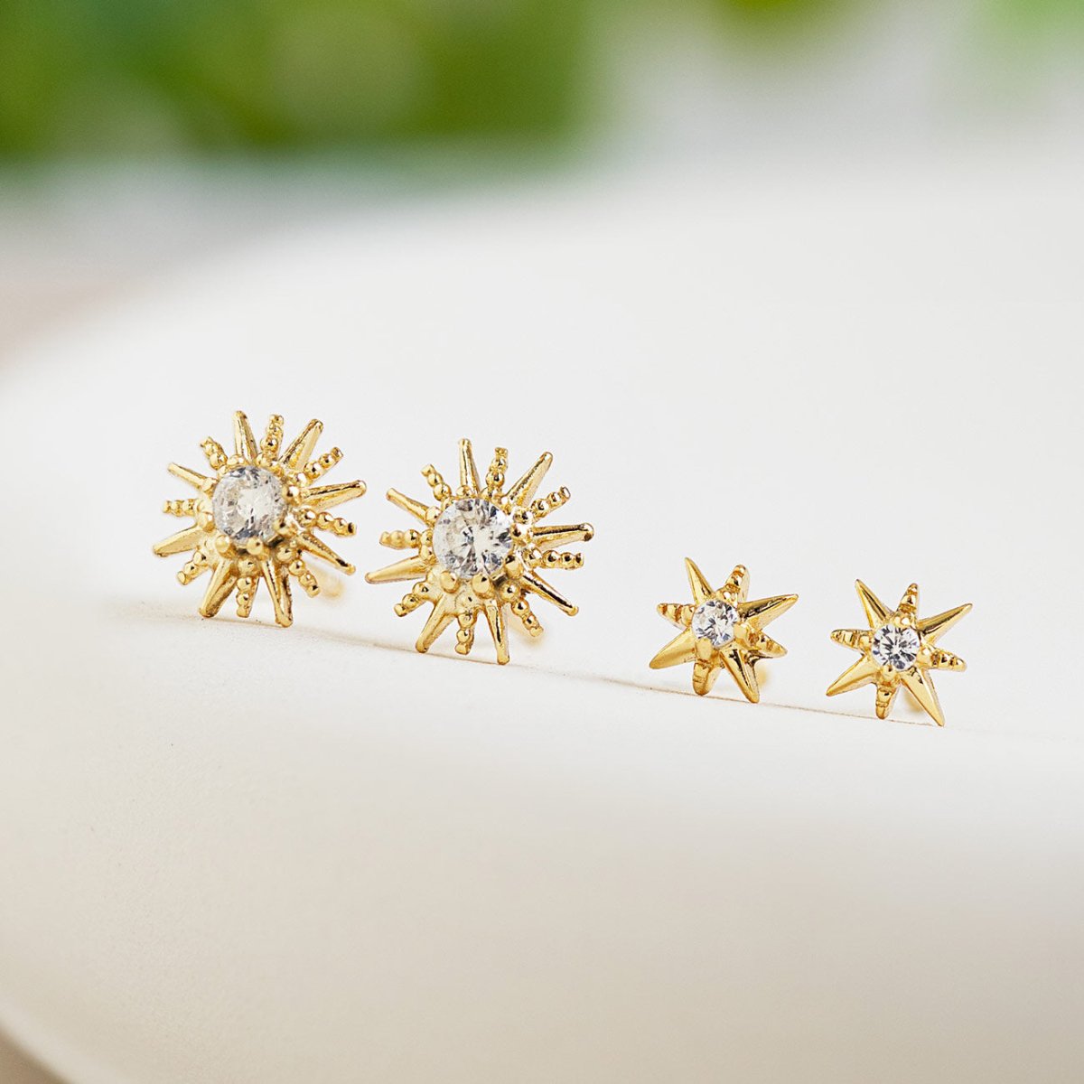 Gold vermeil starburst studs with white zirconia, two sizes shown side by side on a cream background