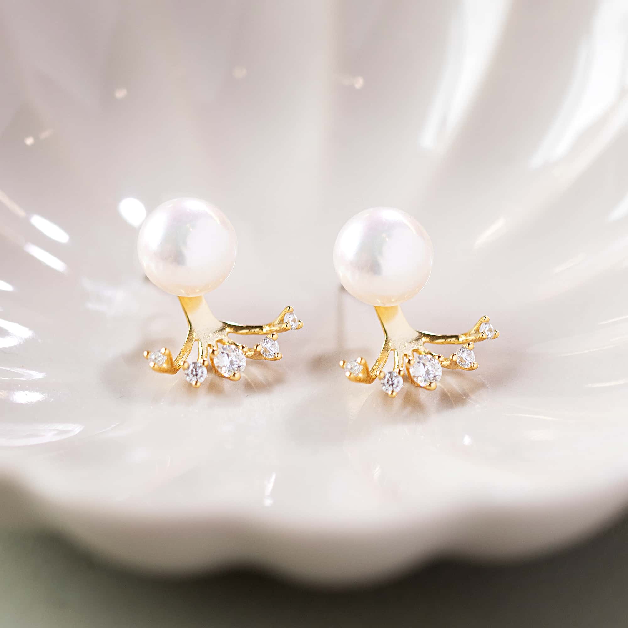 Gold vermeil pearl ear jacket studs with a crystal fan, close-up detail in a shell dish