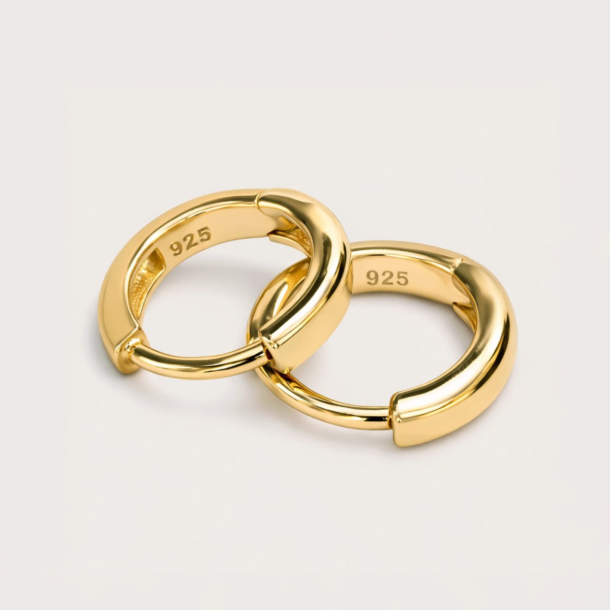 Gold vermeil huggie hoop earrings with hinged bands, close-up detail on a cream background