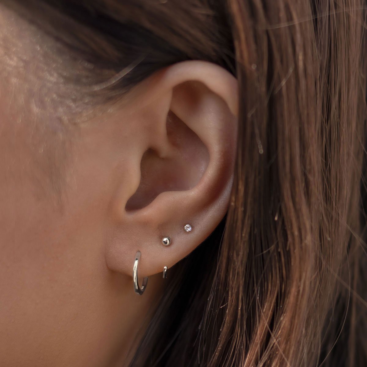 14K white gold open hoop shown on a model's lobe with a beaded stud above
