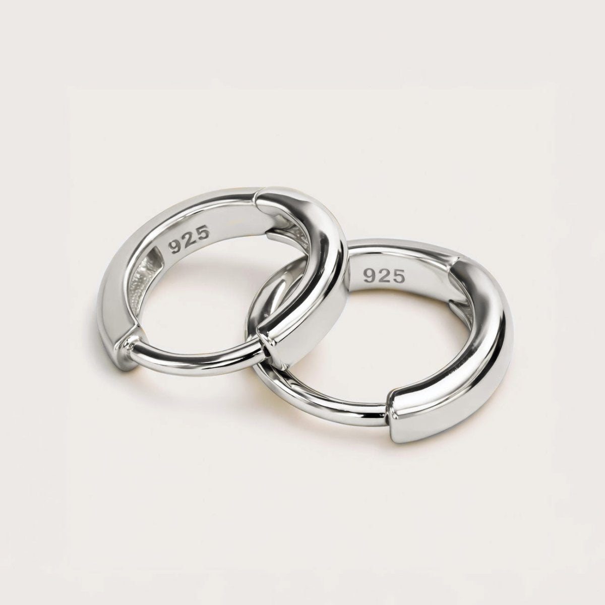Sterling silver huggie hoop earrings with hinged bands, close-up detail on a cream background