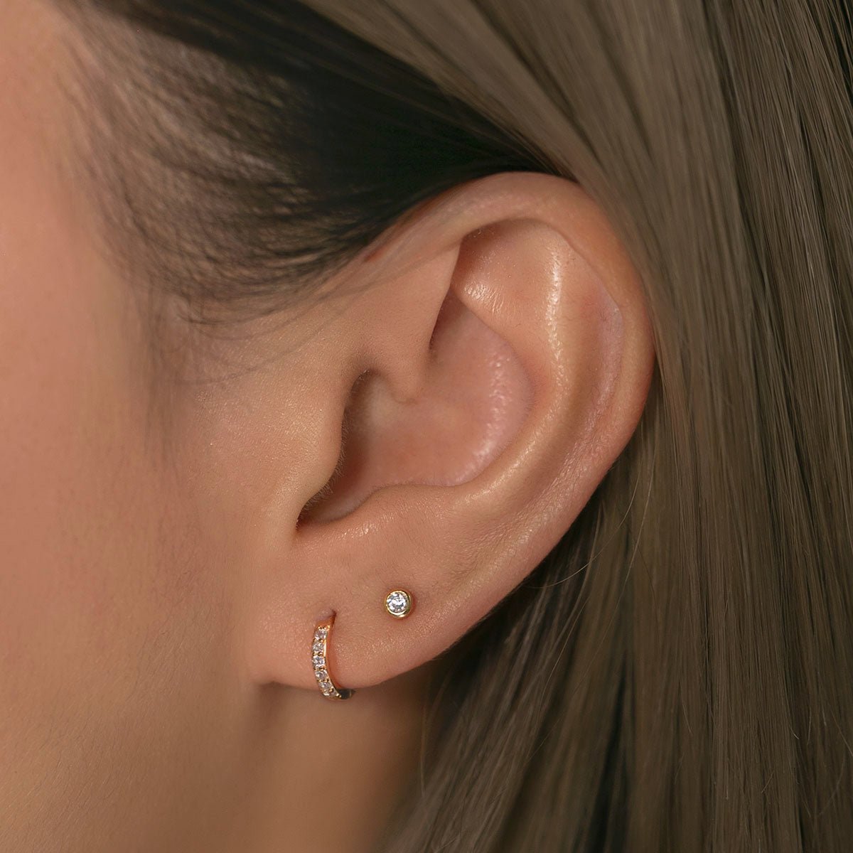 Rose gold vermeil bezel zirconia stud worn on a model's lobe in a layered ear stack