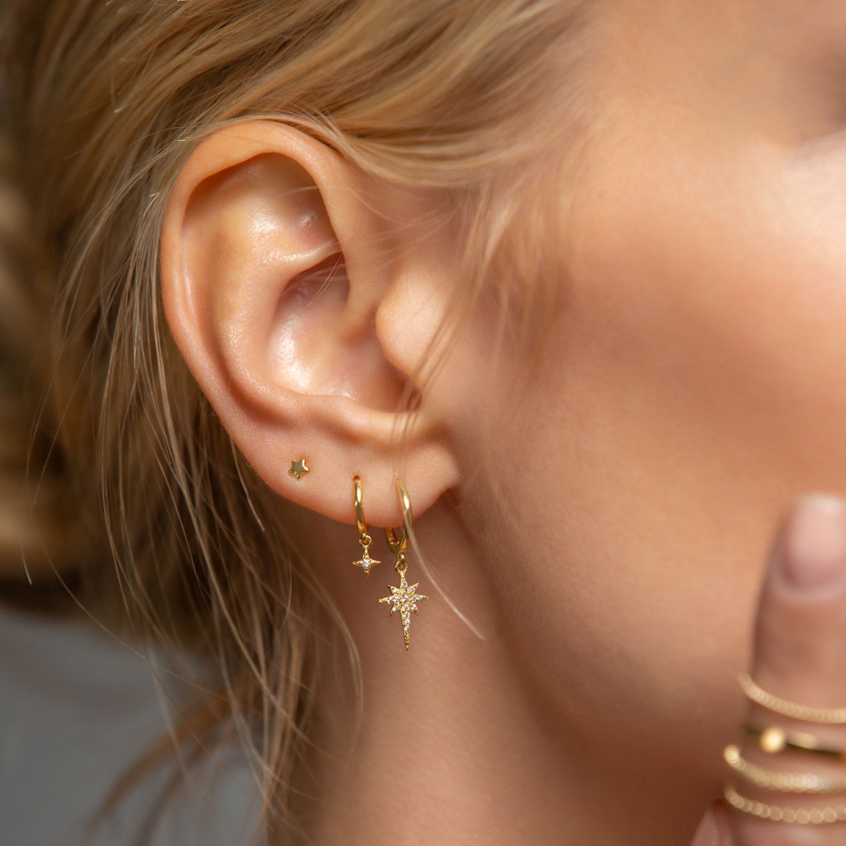 Gold vermeil tiny star lobe stud shown on a model's ear, styled with gold star huggie hoops