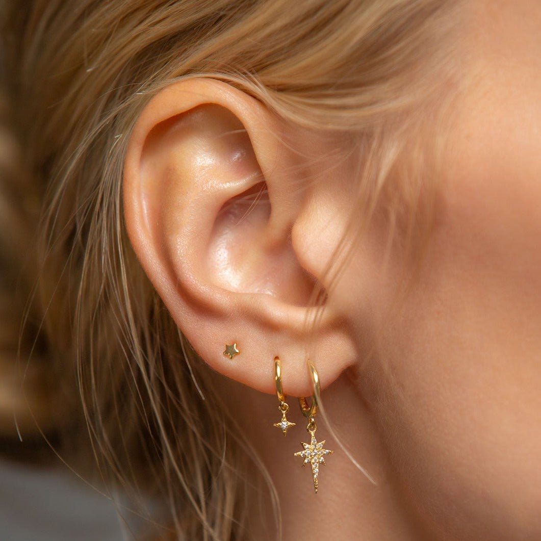 14K gold pavé huggie hoop with a clear-stone starburst charm, shown on a model's lobe