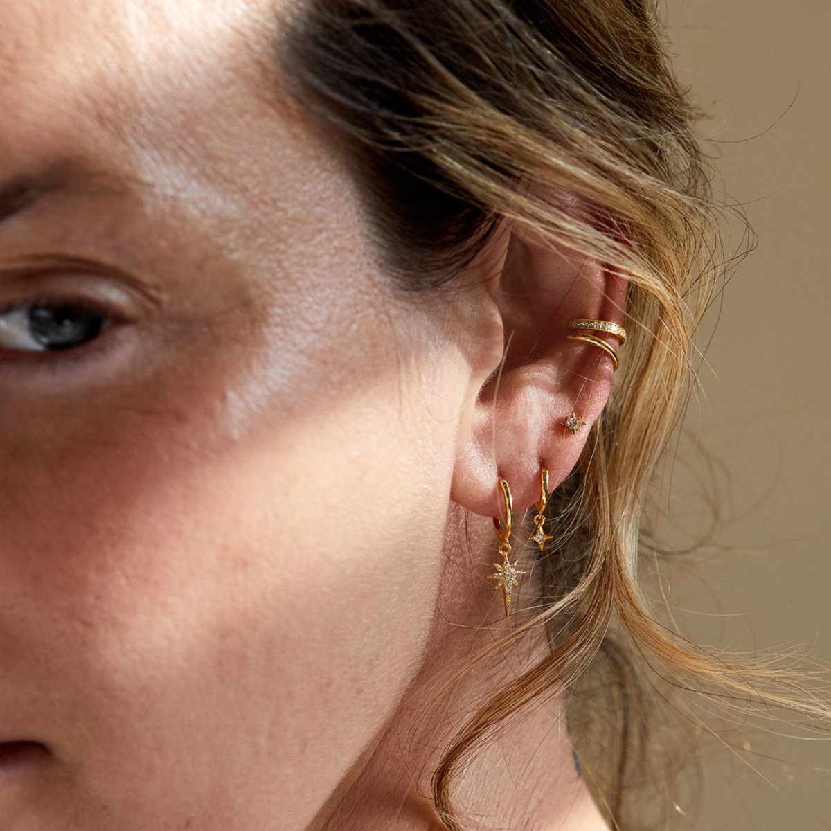 14K gold starburst stud earrings with white zirconia, shown styled on a model's ear stack