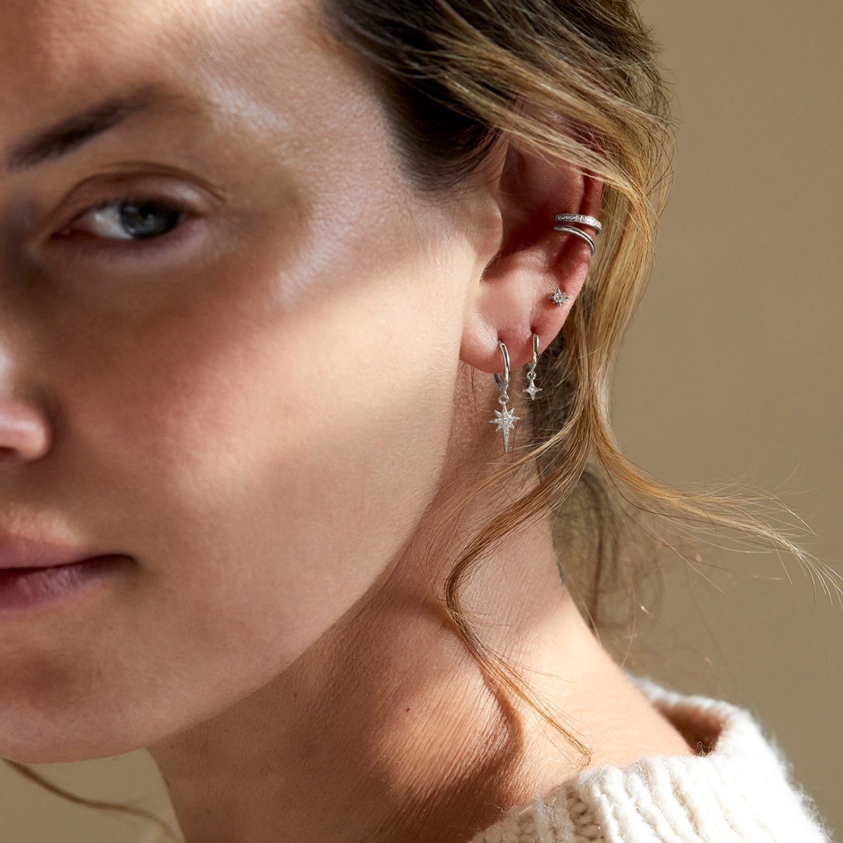 Sterling silver pavé huggie hoop with a clear-stone starburst charm, shown stacked on a model's ear