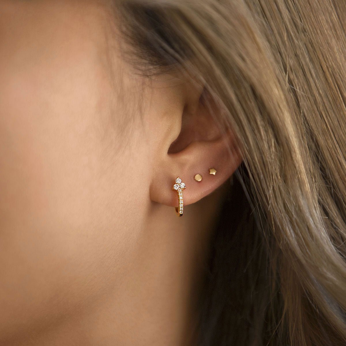 Gold vermeil tiny disc star studs shown on a model's lobe beside a pavé huggie hoop