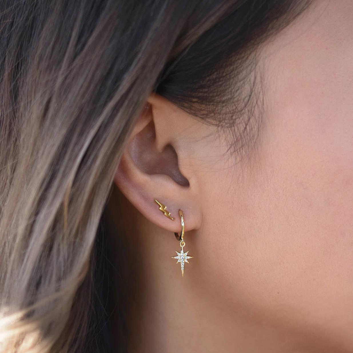 Gold vermeil tiny lightning bolt stud worn on a model's lobe above a starburst drop hoop