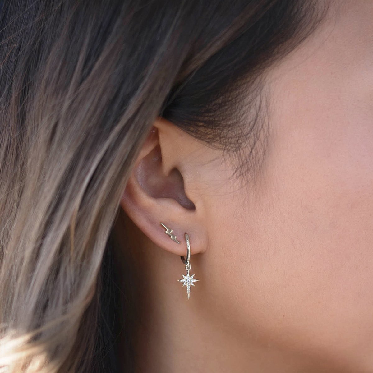 Sterling silver tiny lightning bolt stud worn on a model's lobe above a starburst drop hoop