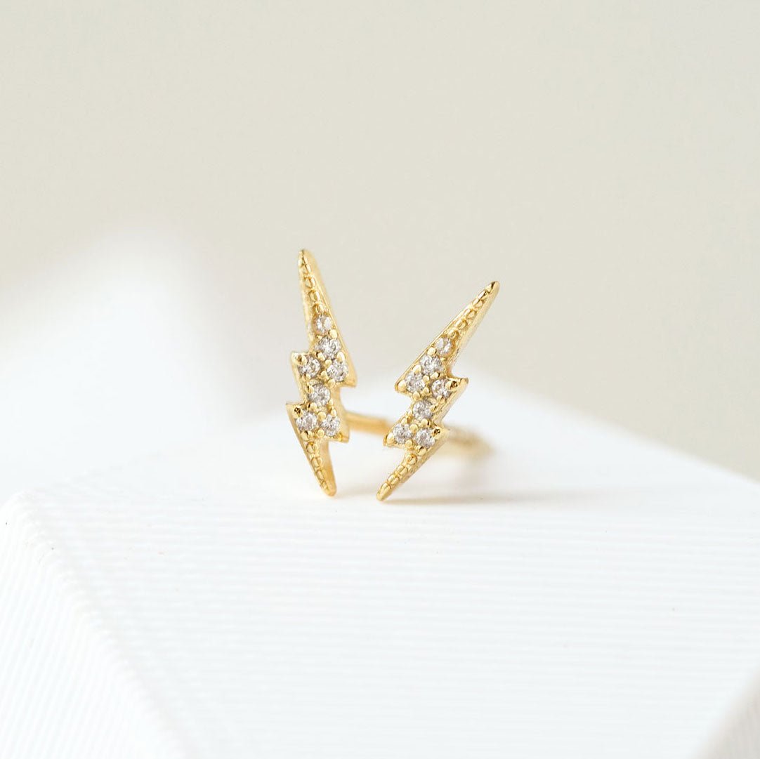 Gold vermeil lightning bolt studs paved with white zirconia, propped on a white surface