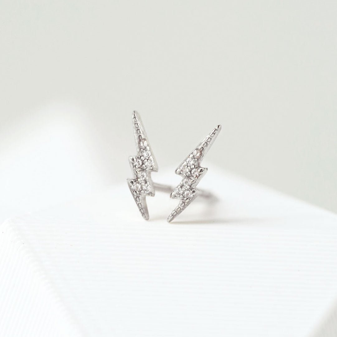 Sterling silver lightning bolt studs paved with white zirconia, propped on a white surface