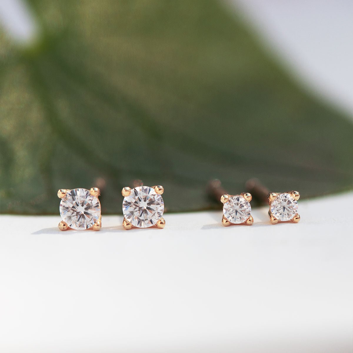 Rose gold vermeil clear zirconia studs in two sizes, shown propped against a green leaf on a white background