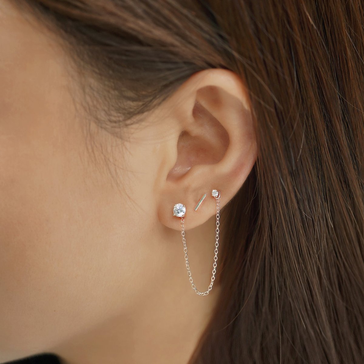 Sterling silver round zirconia stud linked by a chain to a second stud, shown on a model's lobe