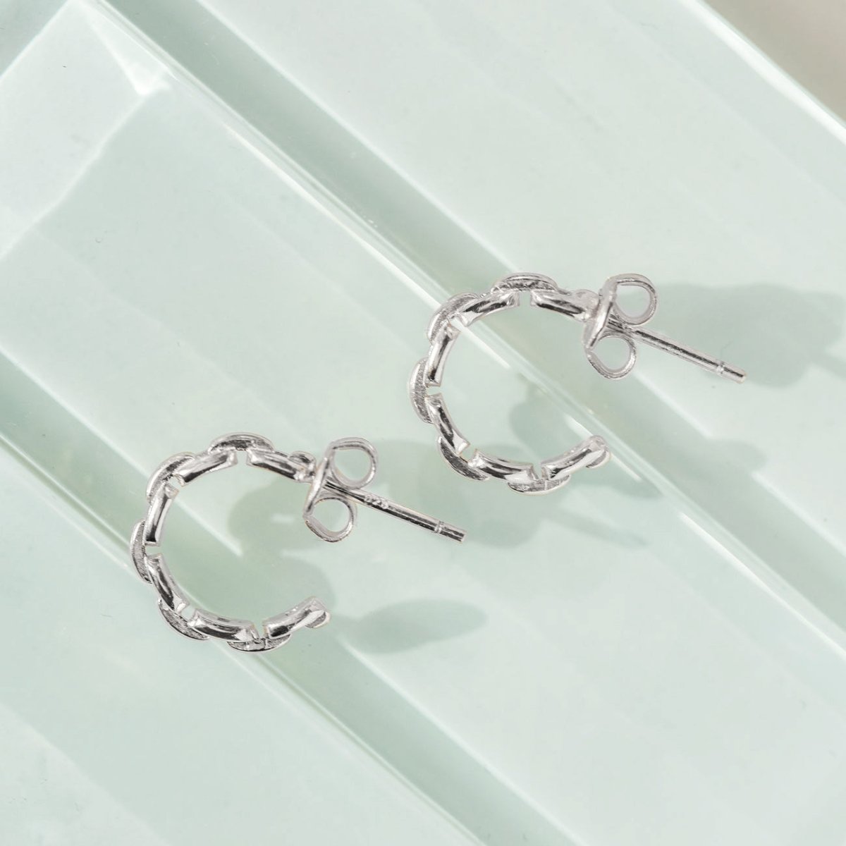 Sterling silver chain-link hoop earrings shown on a pale green surface