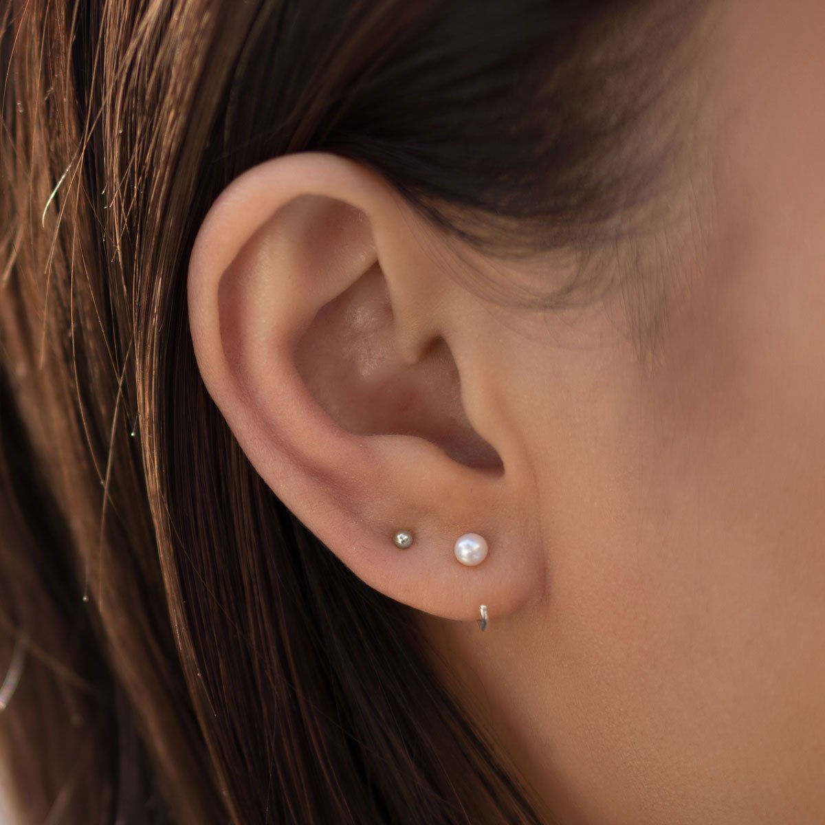 Sterling silver pearl open hug hoop shown on a model's lobe in a small stack