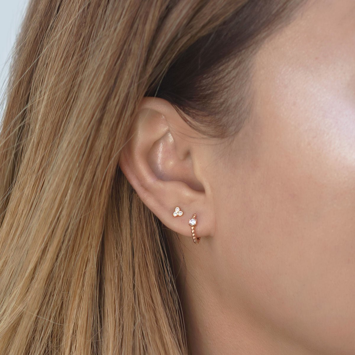 Rose gold vermeil tiny zirconia trio stud shown close-up on a model's lobe