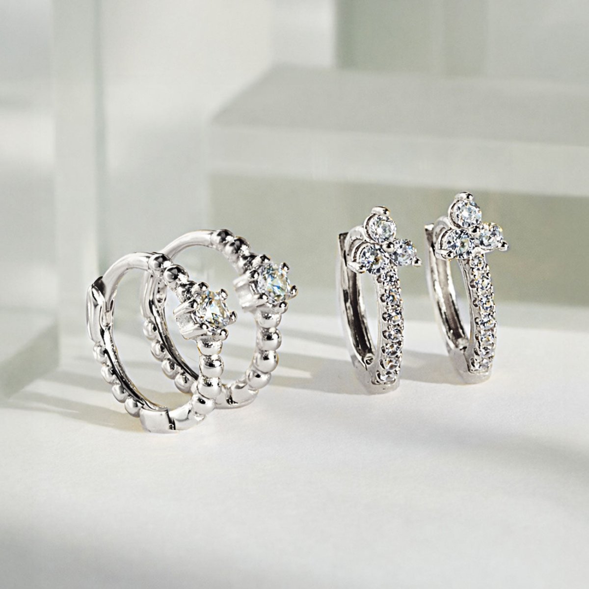 Sterling silver pavé huggie hoops with clear zirconia, shown beside beaded huggies on a white surface