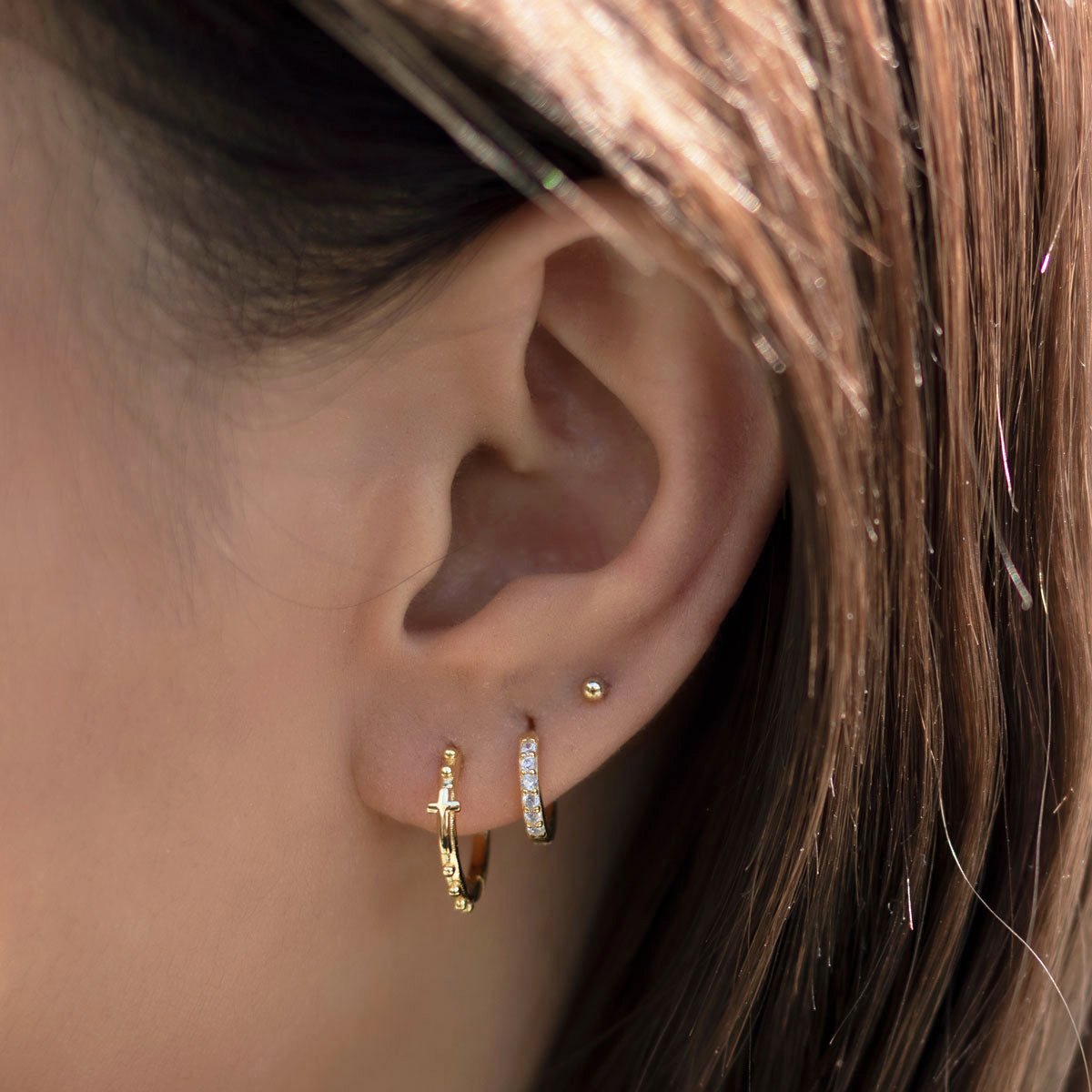 Gold-filled tiny ball studs shown on a model's lobe above a gold huggie hoop