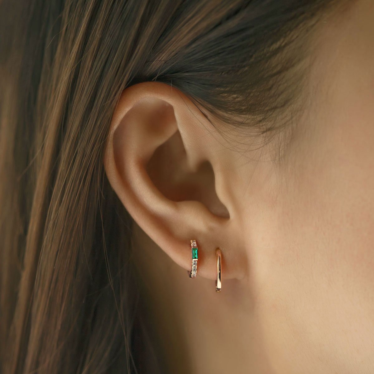 Gold vermeil emerald baguette huggie hoop with white zirconia, shown on a model's lobe with a plain hoop