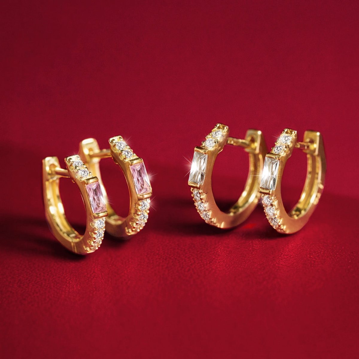 Gold vermeil pink sapphire baguette huggie hoops with white zirconia, shown on a red background