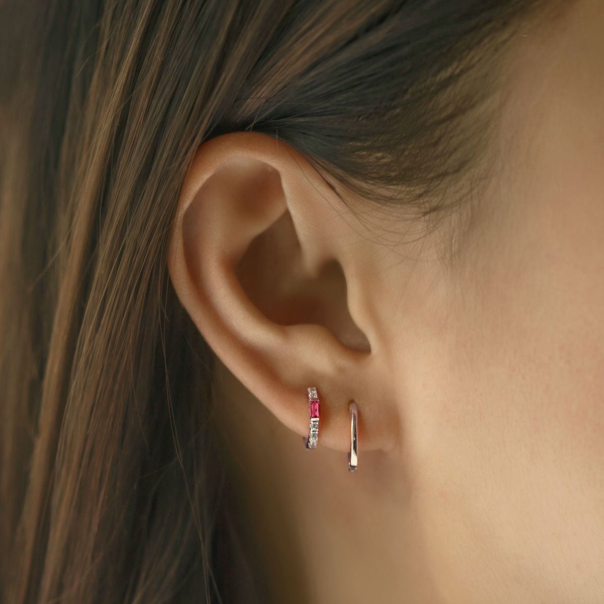 Sterling silver baguette huggie hoop with a red ruby and clear stones, shown on a model's ear