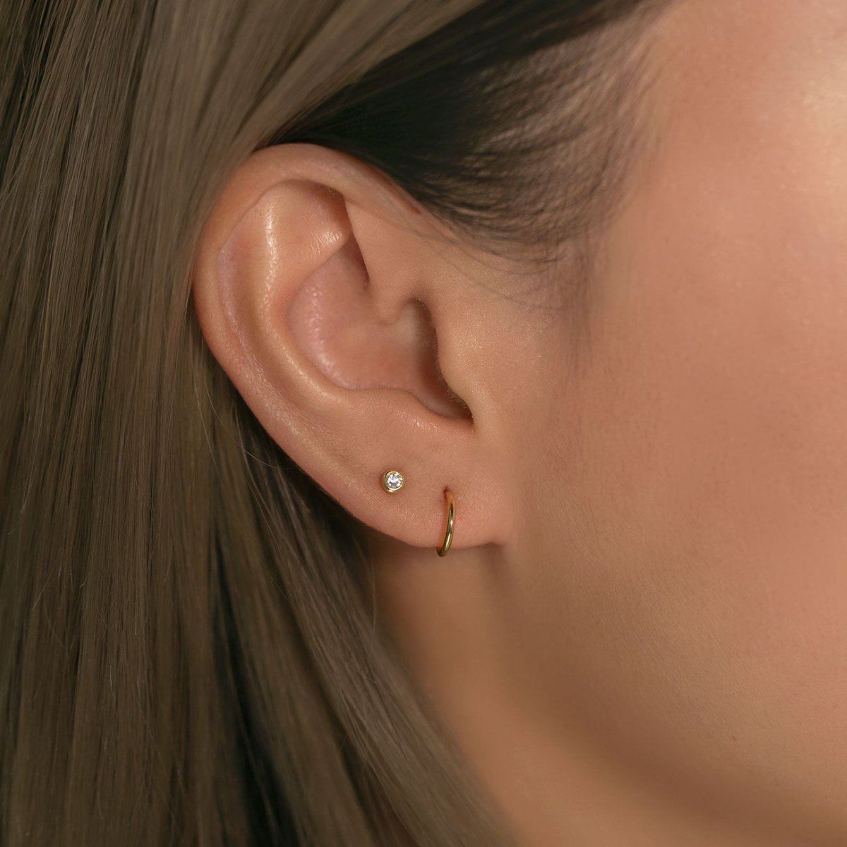 14K gold diamond bezel stud shown on a model's lobe beside a thin gold hoop