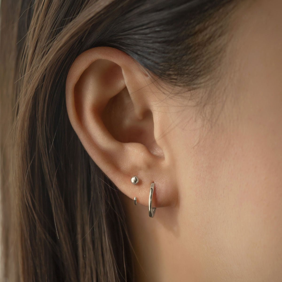 14K white gold sphere stud and plain huggie hoop shown stacked on a model's lobe