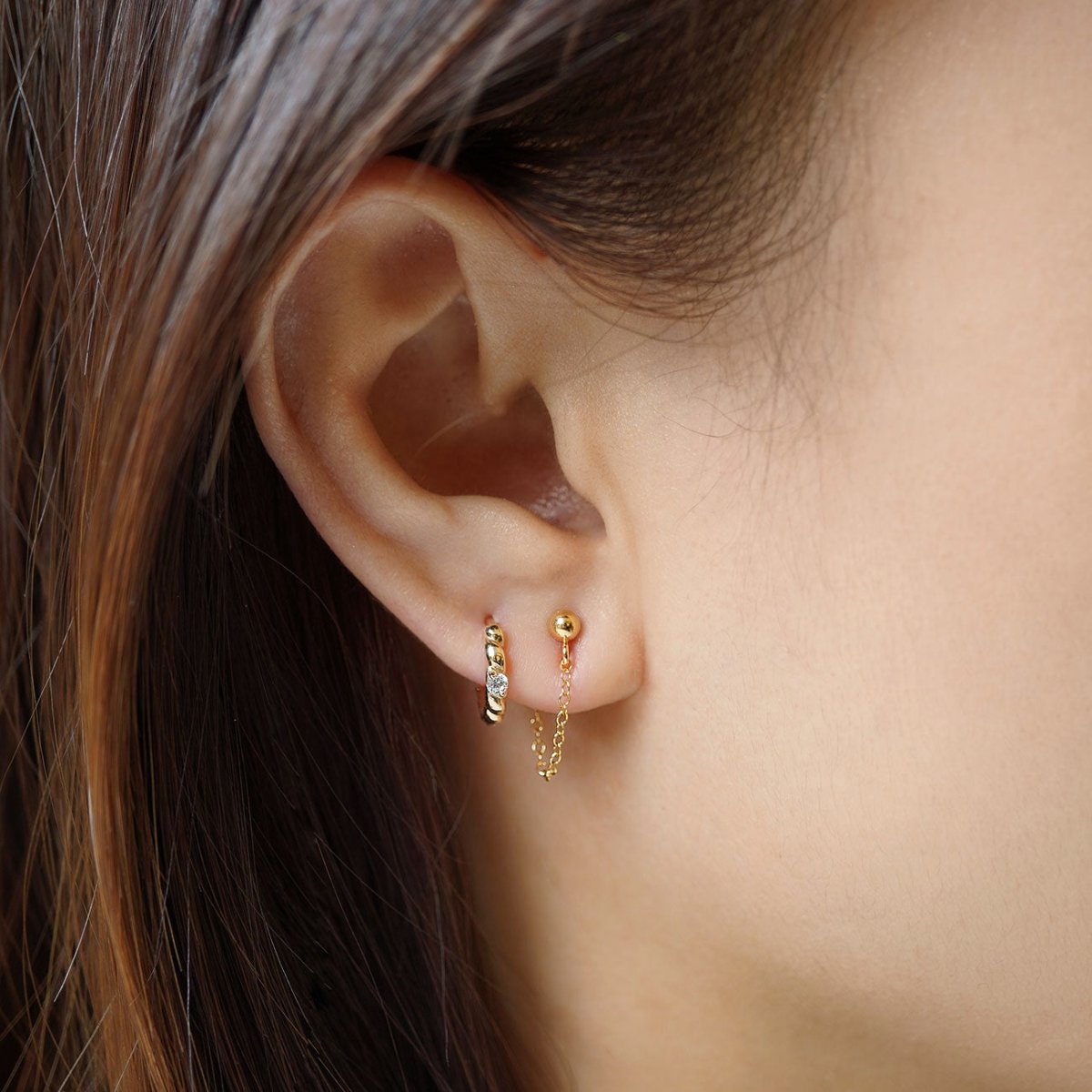 Gold vermeil ball-stud earring with a draped chain shown on a model's lobe in an ear stack